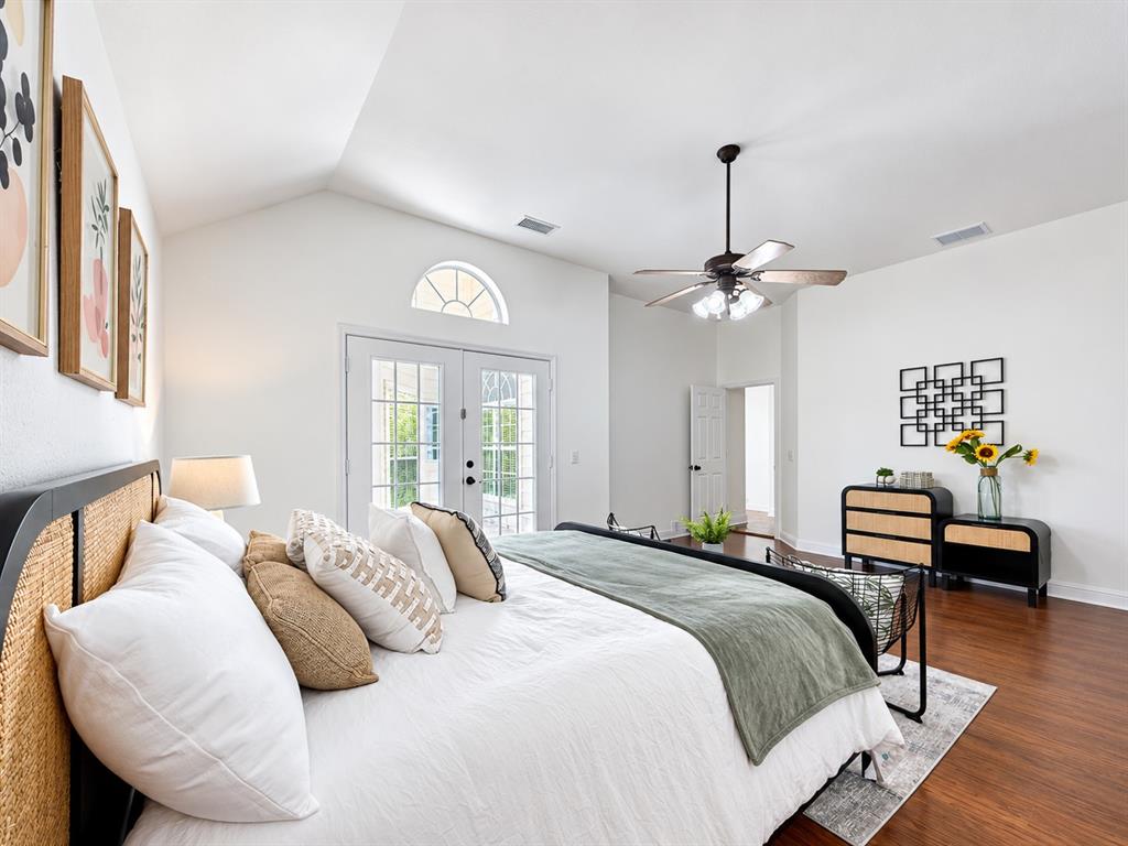 Vaulted ceilings, wood-finish flooring, glass-paneled double doors with an arched transom, and a central ceiling fan with integrated lighting