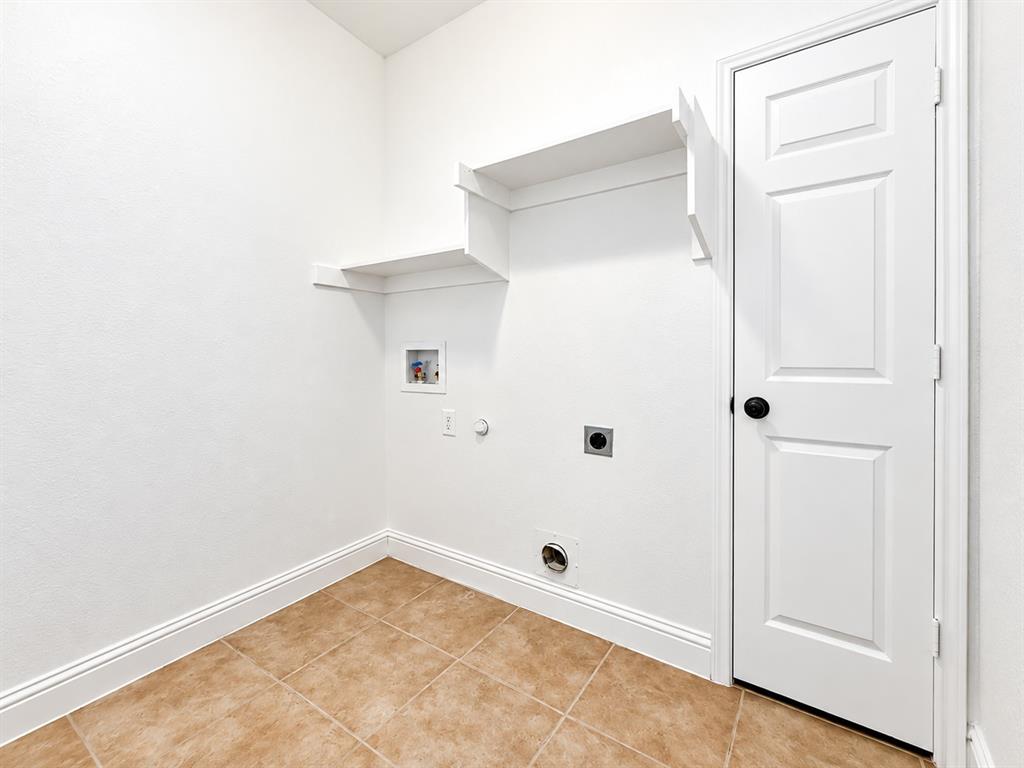 Utility area featuring ceramic tile flooring, built-in wall shelving, and a six-panel door with matte black hardware