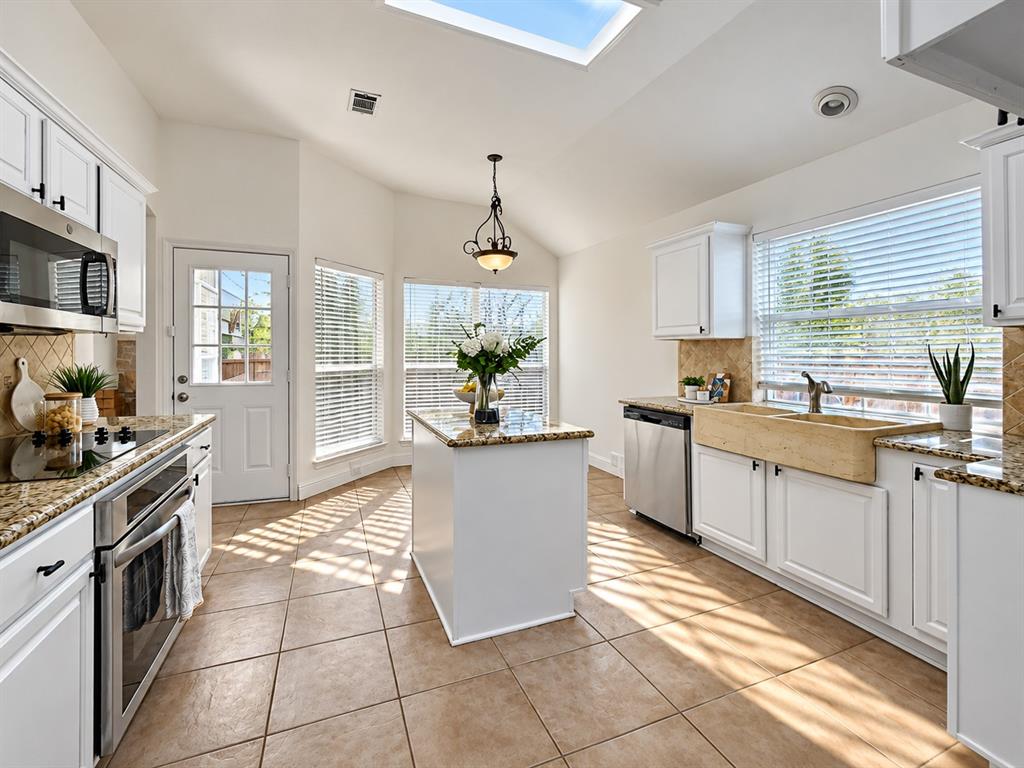Kitchen featuring white cabinetry, stone-surface countertops, central island, farm-style sink, and skylight