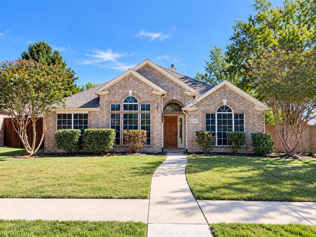 Brick exterior featuring a gabled roofline, arched window detailing, wood-finish front door, and manicured landscaping