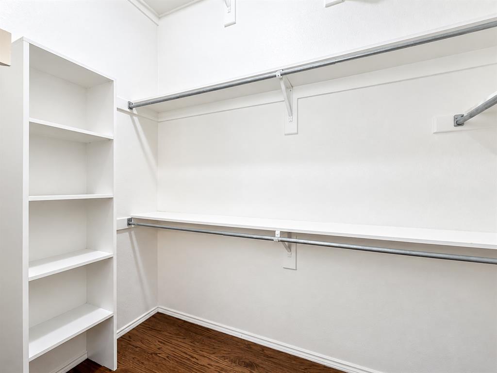 Built-in vertical shelving unit with wood-finish flooring and tiered metal garment rods