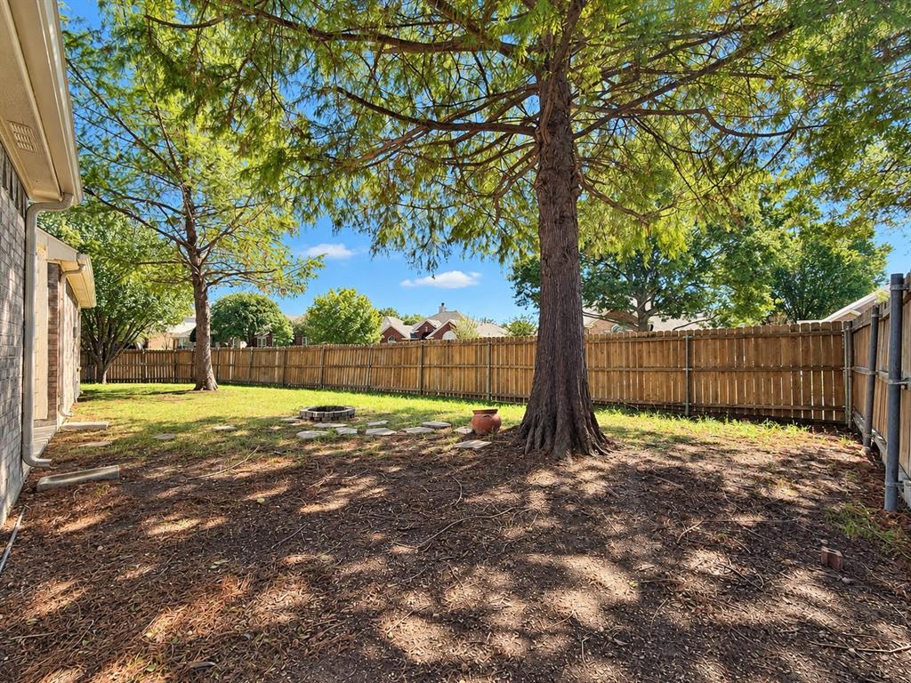 Rear yard featuring mature trees, wood privacy fencing, a stone-bordered fire pit, and stone hardscaping