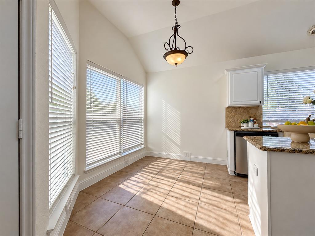 Vaulted ceilings, expansive windows with horizontal blinds, tiled flooring, ornate pendant lighting, and stone-finish countertops with tile backsplash