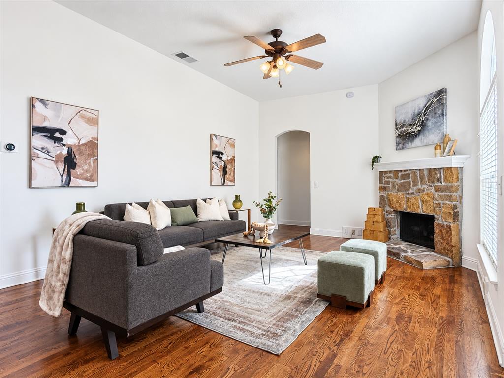 Living area featuring high ceilings, wood-finish flooring, stone-surround fireplace with mantel, and arched entryway