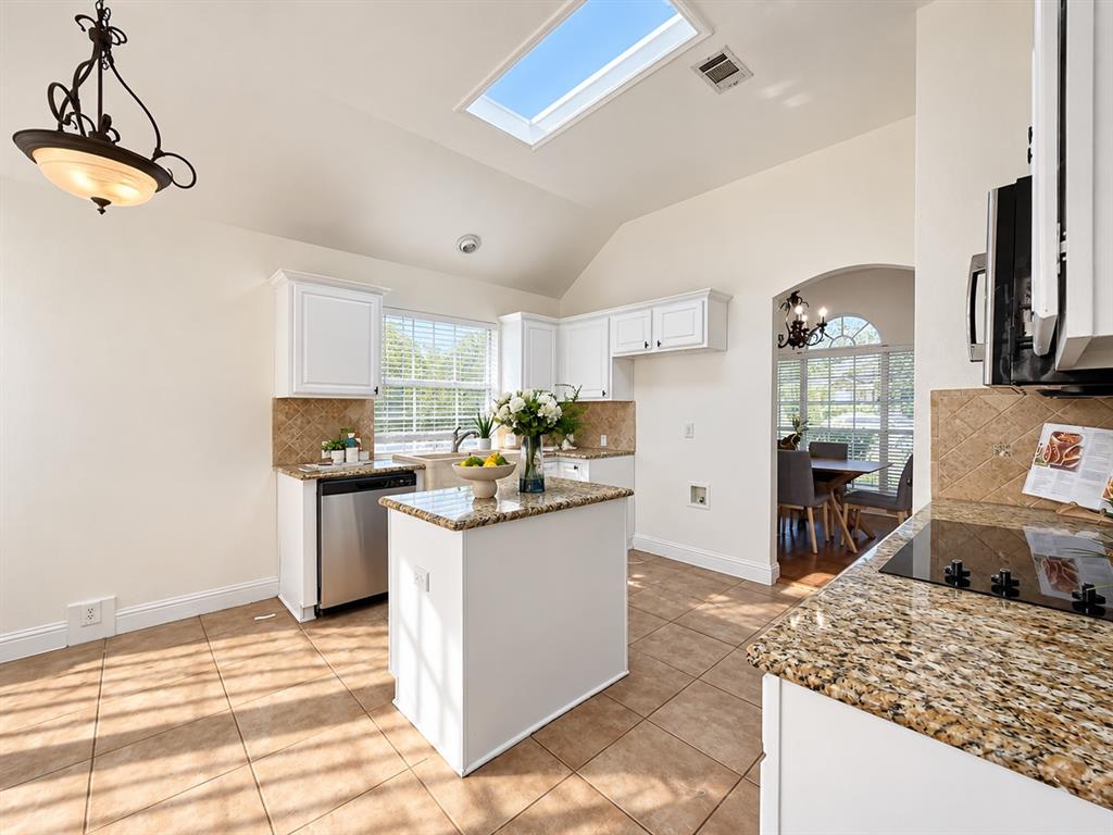 Kitchen featuring white cabinetry, stone countertops, central island, skylight, and ceramic tile flooring