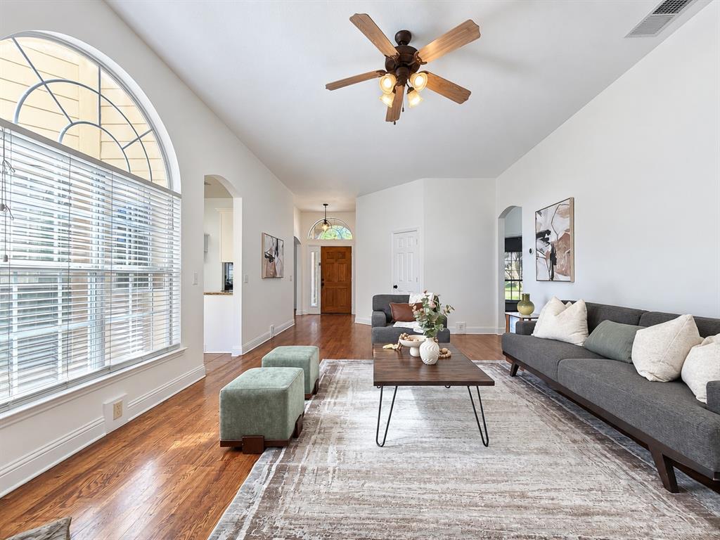 Living area featuring wood-finish flooring, a large arched window with horizontal blinds, a vaulted ceiling, and a ceiling fan with integrated light fixtures