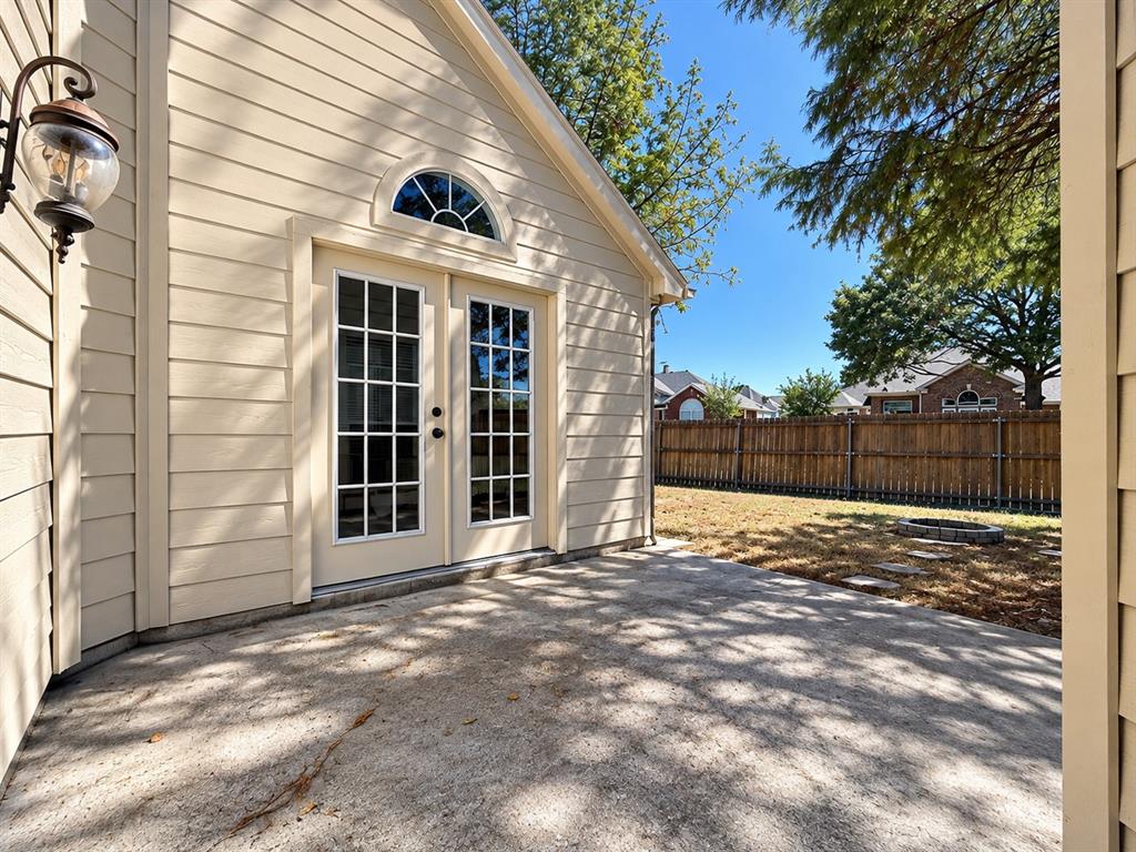 Concrete patio featuring double French glass doors, a semi-circular transom window, exterior lantern-style wall lighting, and wood-toned lap siding