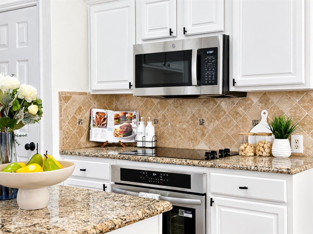 Kitchen featuring white shaker-style cabinetry, stone countertops, a diagonal-set stone tile backsplash, stainless steel built-in microwave, and a glass-top electric range