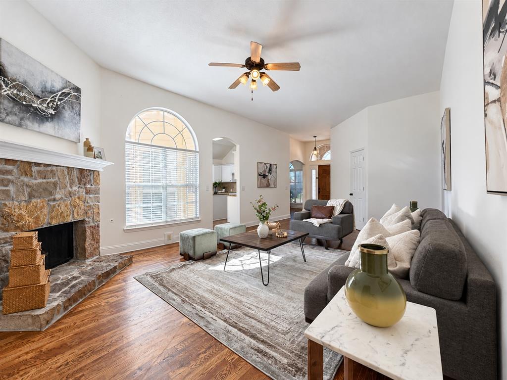 Living area featuring a floor-to-ceiling natural stone fireplace, arched window with a grid design, wood-finish flooring, vaulted ceiling with a central fan, and an arched entry