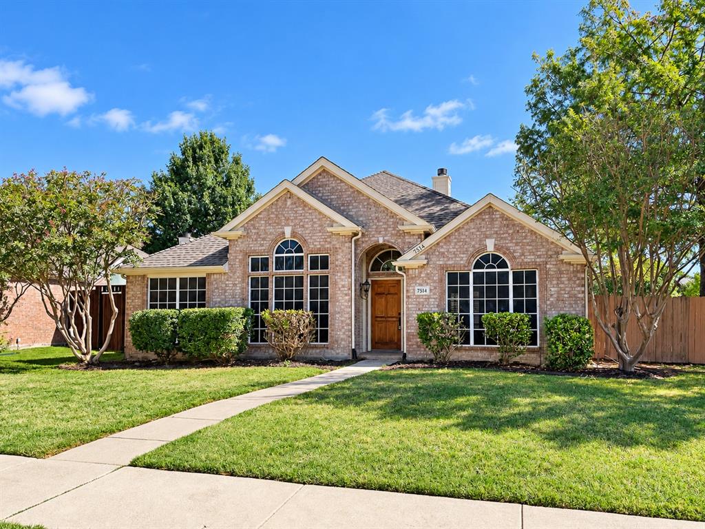 Brick exterior featuring an arched entryway, grid-pattern windows, and a multi-gabled roofline, complemented by a front lawn and mature landscaping