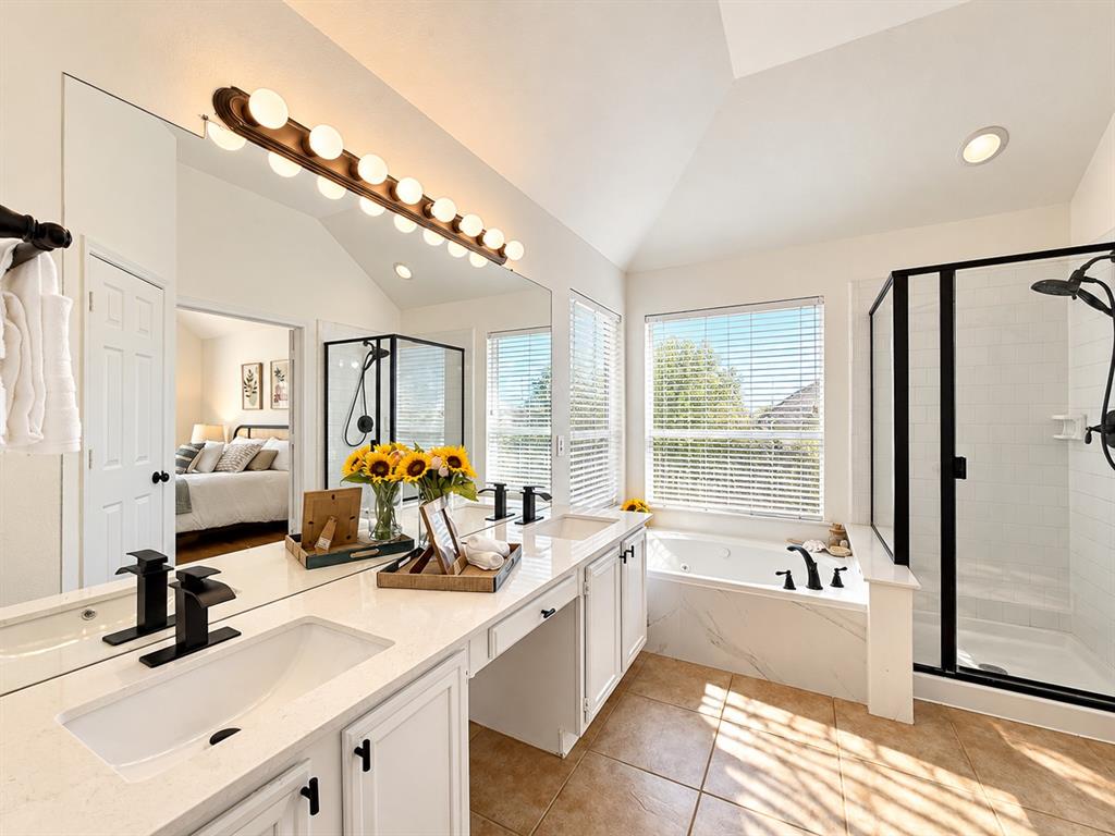 Double vanity featuring white cabinetry, quartz countertops, undermount sinks with matte black fixtures, an oversized mirror, and a separate soaking tub and shower enclosure with matching matte black hardware