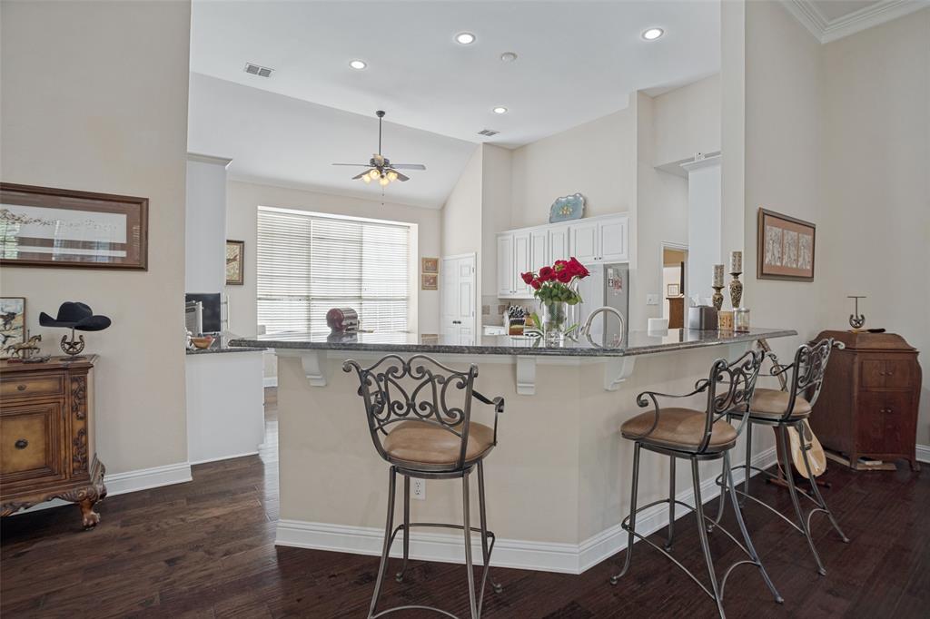 Interior featuring dark wood-finish flooring, vaulted ceilings with recessed lighting, and a raised countertop peninsula with decorative corbels and a sink Breakfast bar