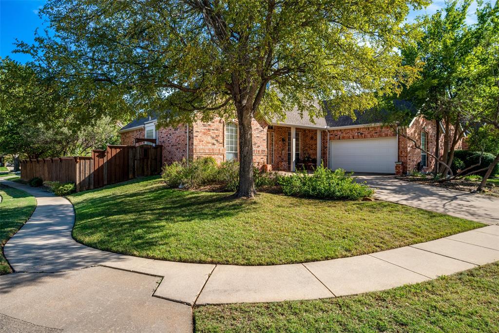 Brick exterior with a covered entryway, attached garage, concrete driveway, and mature landscaping