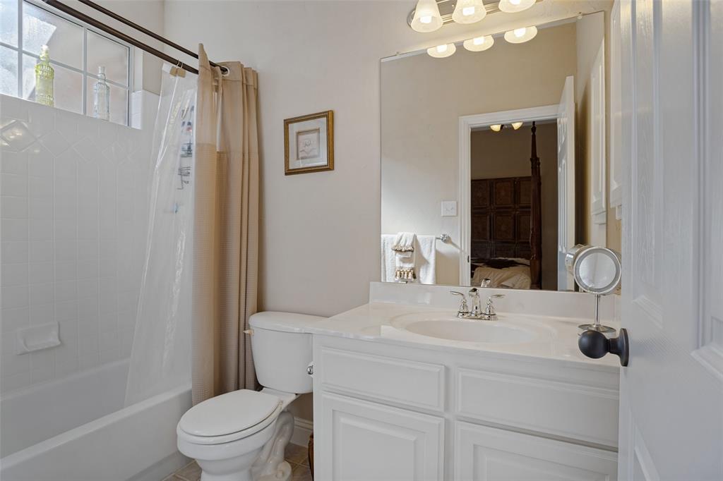 Bathroom featuring a vanity with an integrated basin, a large wall-mounted mirror, multi-bulb overhead lighting, a shower-tub combination with tile surround, and an upper transom window