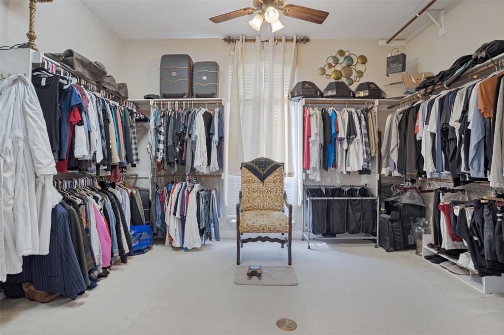Customized dressing area featuring extensive wall-mounted shelving, integrated hanging rods, a ceiling fan with light fixture, and a central window with drapery hardware