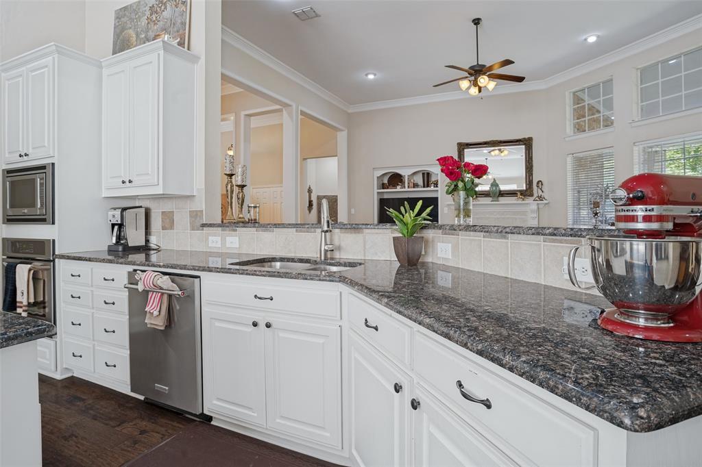 Kitchen featuring white shaker-style cabinetry, dark stone countertops, stainless steel dishwasher, built-in microwave and wall oven, and wood-finish flooring