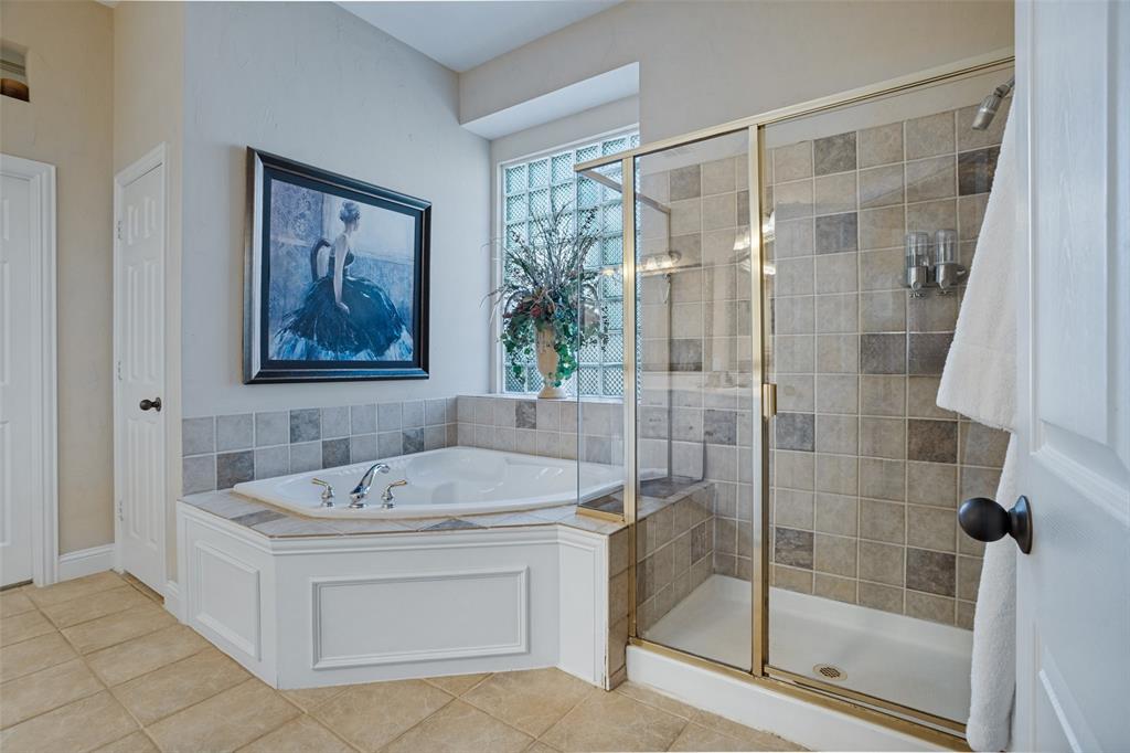 Corner soaking tub with tile surround, glass block window, and walk-in shower featuring a brass-tone frame and multi-tonal square wall tile