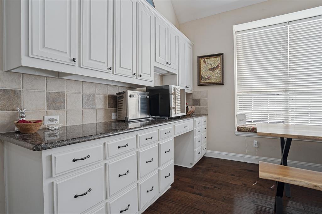 White cabinetry with dark hardware, stone-finish countertops, square tile backsplash, built-in desk area, and wood-finish flooring