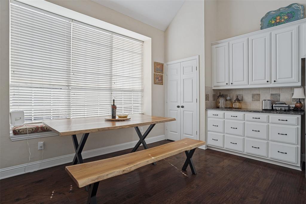 Kitchen featuring vaulted ceilings, white cabinetry, dark stone-finish countertops, tile backsplash, and wood-finish flooring