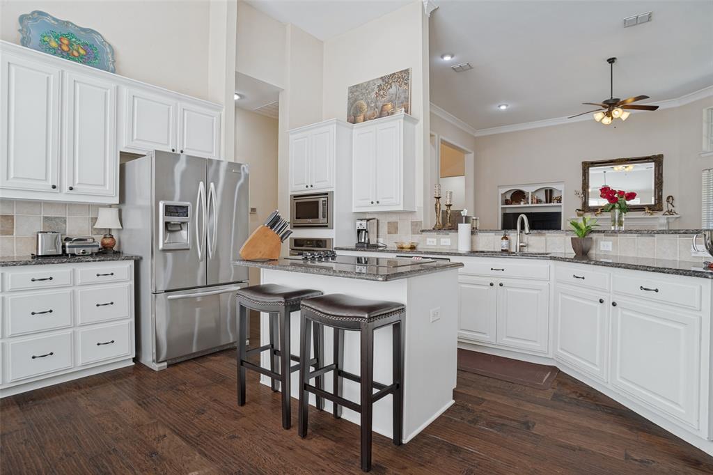 Kitchen featuring white cabinetry, dark stone countertops, stainless steel appliances, a central island with counter seating, and wood-finish flooring