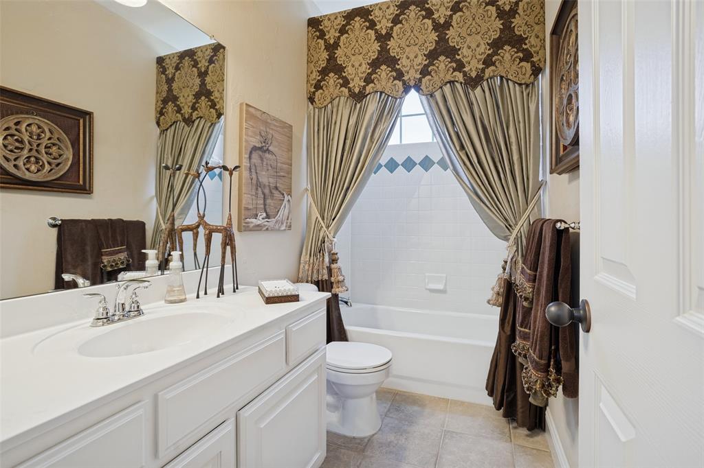 Bathroom featuring a white vanity cabinet with an integrated sink, polished chrome faucet, large vanity mirror, tile flooring, and a tub-shower combination with tile surround