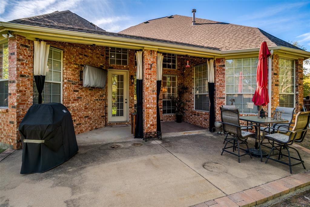 Covered brick patio featuring a concrete floor, stone-trimmed border, and glass-paneled door