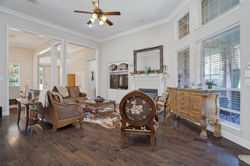 High-ceiling living area featuring dark wood-finish flooring, a built-in fireplace with an ornate mantel, multi-pane transom windows, and crown molding