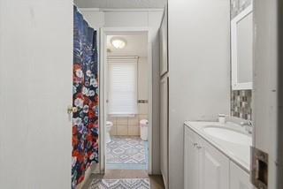 Bathroom featuring a vanity with integrated sink, stone-finish countertop, decorative tile backsplash, and full-height built-in storage cabinetry Bathroom featuring a vanity with integrated sink, stone-finish countertop, decorative tile backsplash, and full-height built-in storage cabinetry