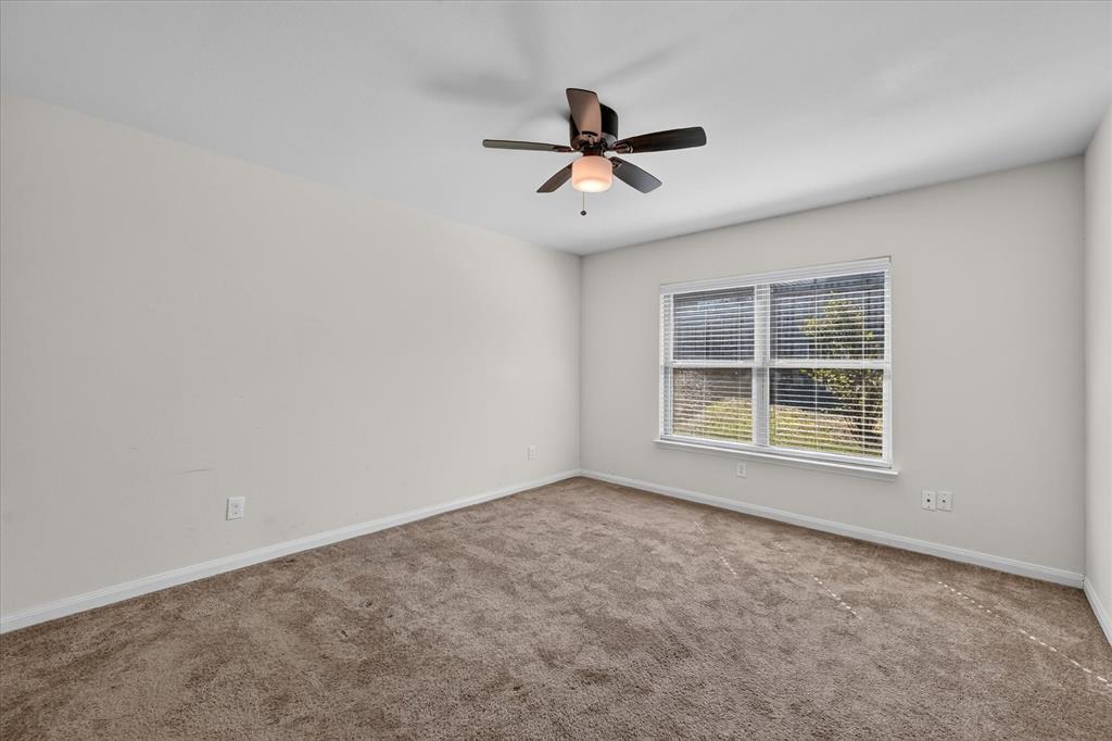 Neutral-toned wall interior featuring plush wall-to-wall carpeting, a multi-blade ceiling fan with an integrated light fixture, and a dual-pane window