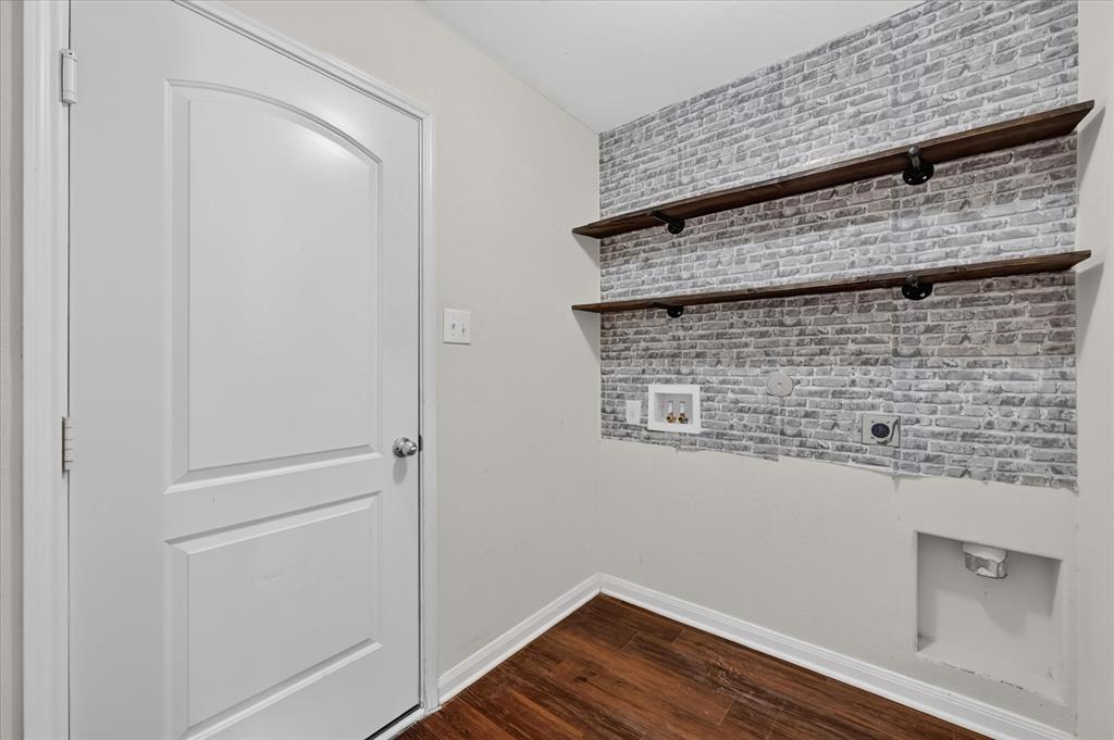 Utility area featuring wood-finish flooring, two open industrial-style floating shelves, and decorative faux-brick wall paneling