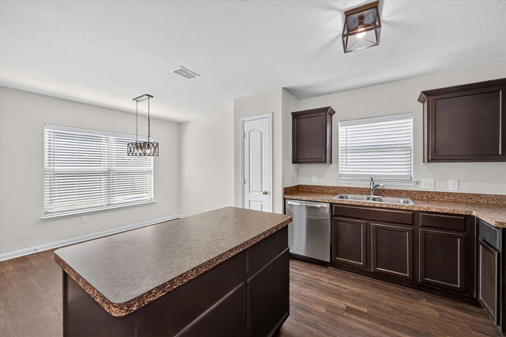 Kitchen featuring dark cabinetry, expansive countertops, a central island, stainless steel dishwasher, and wood-finish flooring