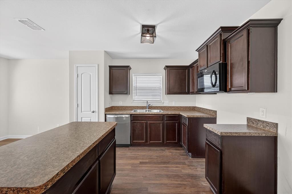 Kitchen featuring dark-finish cabinetry, an island with countertop seating, stone-patterned laminate countertops, stainless steel appliances, and wood-finish flooring