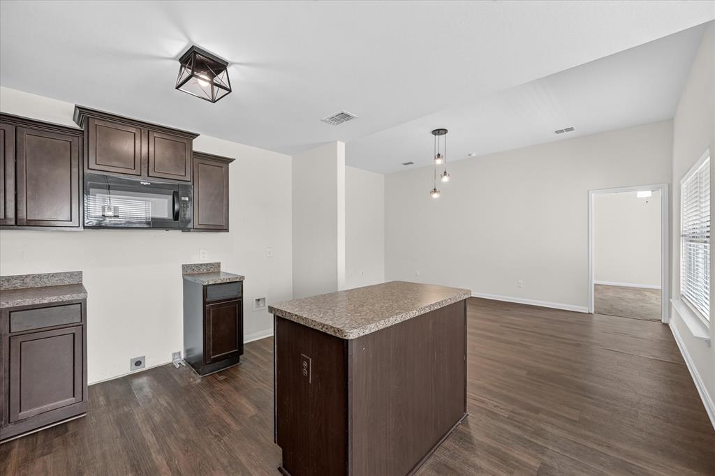 Kitchen featuring dark-finish cabinetry, stone-texture countertops, wood-finish flooring, a center island, and overhead pendant lighting