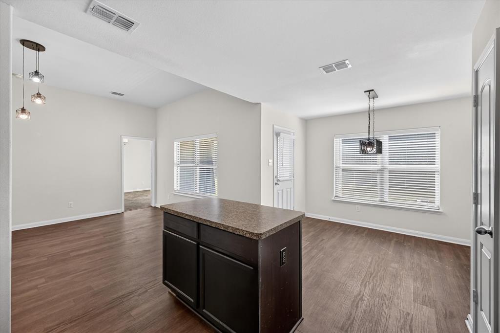 Wood-finish flooring, central kitchen island with a stone-composite countertop, dark-finish cabinetry, and decorative pendant lighting