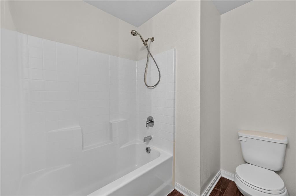 White acrylic tub and shower combination with a chrome handheld shower head, matching single-handle faucet, and wood-finish flooring