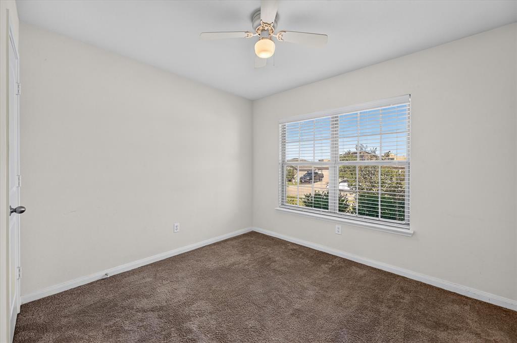Neutral-toned interior featuring wall-to-wall carpeting, a multi-pane window with installed blinds, and a central ceiling fan with an integrated light fixture