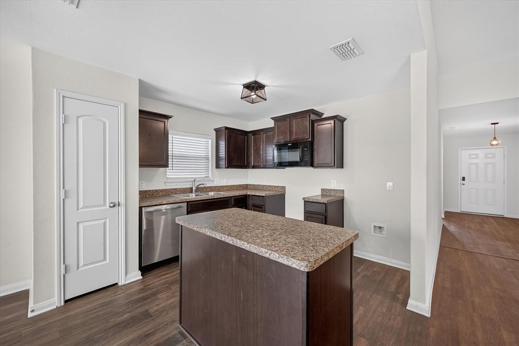 Kitchen featuring dark wood-finish cabinetry, a center island, stone-finish countertops, stainless steel appliances, and wood-finish flooring Kitchen featuring dark wood-finish cabinetry, a center island, stone-finish countertops, stainless steel appliances, and wood-finish flooring