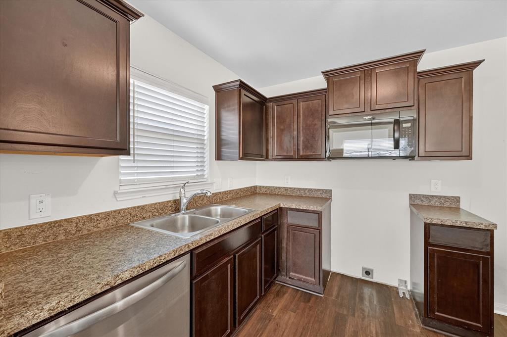 Kitchen featuring dark-finish cabinetry, stone-texture laminate countertops, stainless steel dual-basin sink, integrated over-the-range microwave, and wood-finish flooring