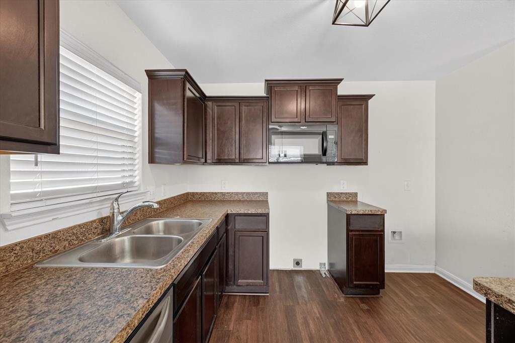 Dark-finish cabinetry paired with speckled laminate countertops, dual-basin stainless steel sink, built-in microwave, and wood-finish flooring