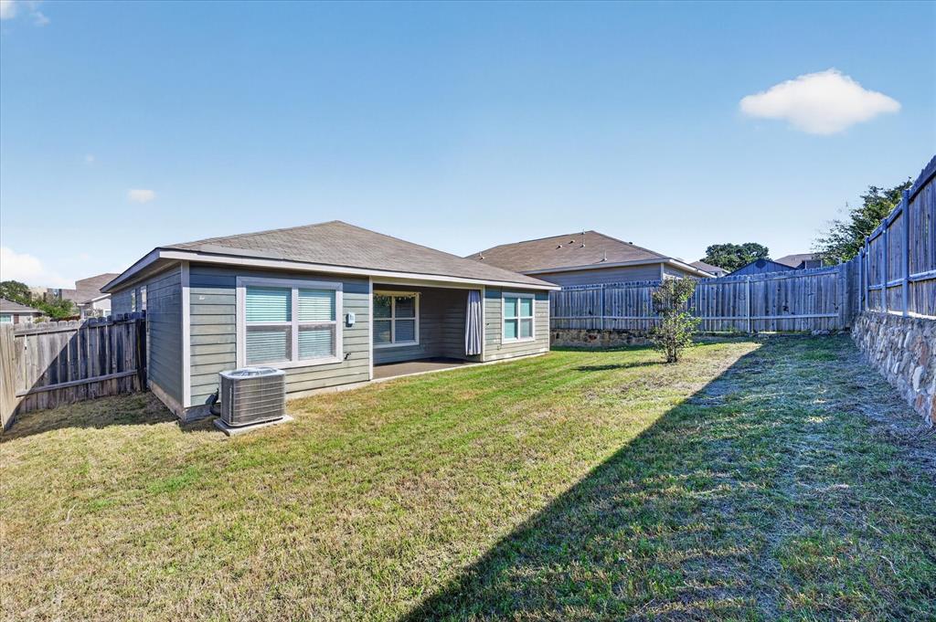 Rear exterior featuring horizontal lap siding, a covered patio, and a tiered retaining wall with stone-finish accents enclosed by wood fencing
