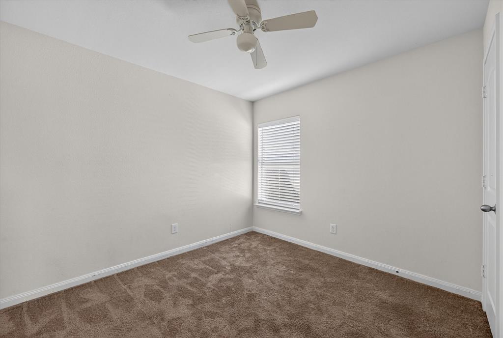Neutral-toned interior space featuring neutral wall-to-wall carpeting, a multi-blade ceiling fan, and a single window with horizontal blinds