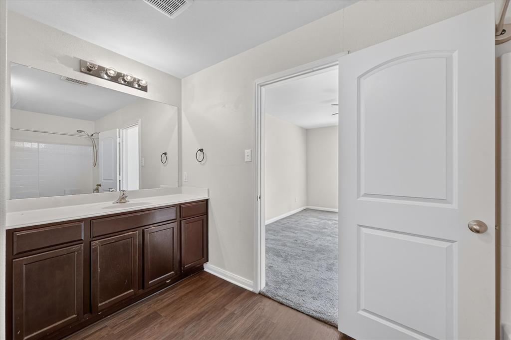Bathroom featuring a dark wood-finish vanity, solid-surface countertop, full-width vanity mirror, and wood-finish flooring