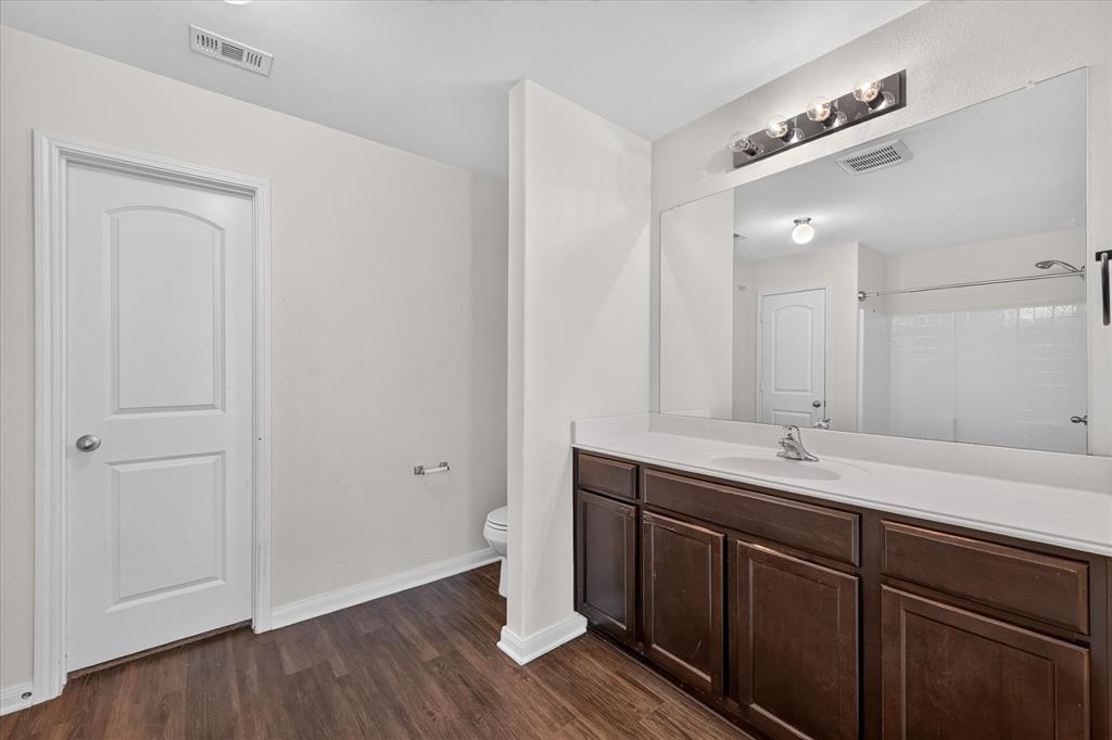 Bathroom featuring a dark wood-finish vanity, a full-width wall mirror, wood-finish flooring, and a single-basin countertop