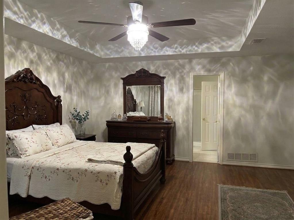 Tray ceiling featuring a central crystal-accented chandelier with integrated ceiling fan and wood-finish flooring