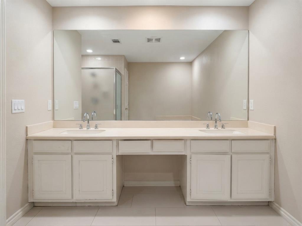 Double vanity featuring white cabinetry, a solid-surface countertop with dual integrated sinks, polished chrome faucets, and an expansive wall-to-wall mirror