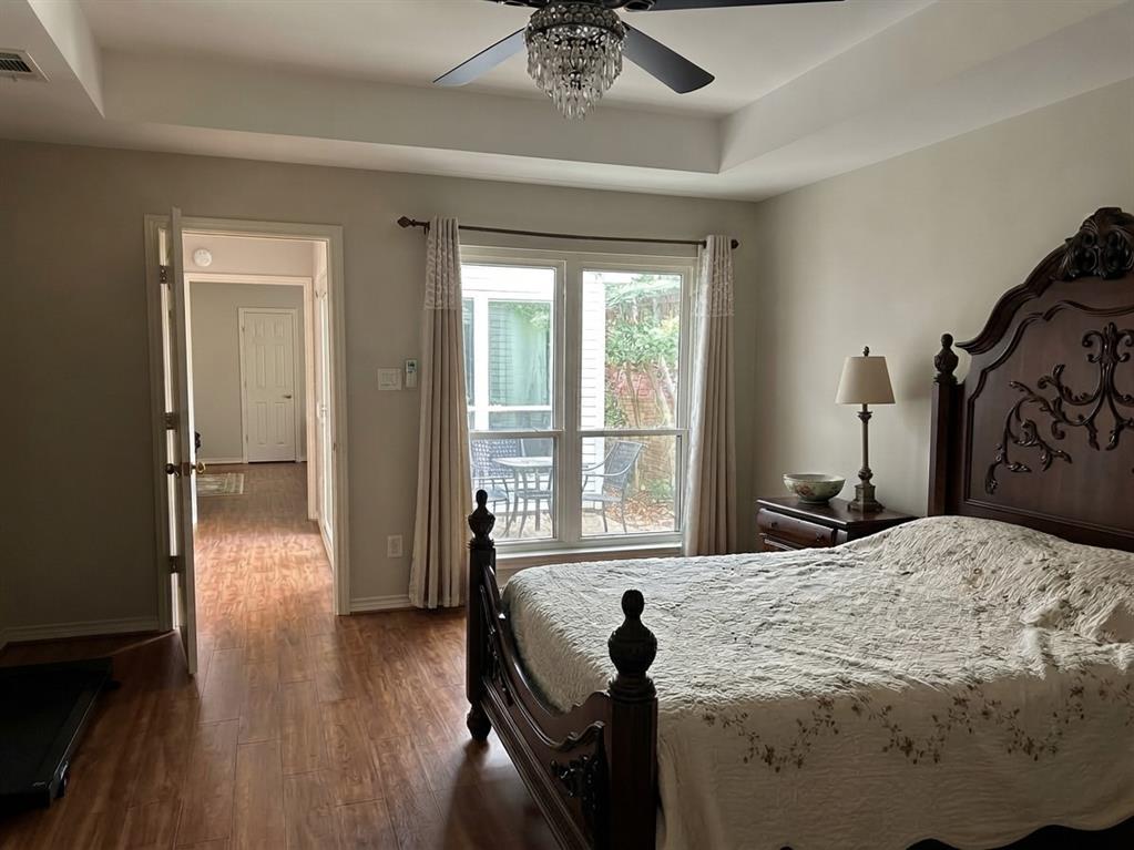 Tray ceiling featuring a central crystal-accented ceiling fan, wood-finish flooring, and large windows with exterior patio exposure