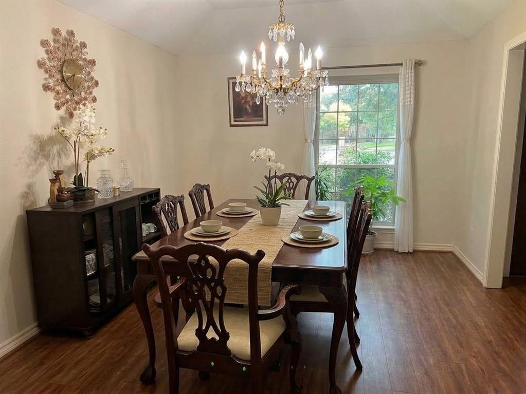 Vaulted ceiling featuring an ornate crystal chandelier, wood-finish flooring, and a large grid-pattern window