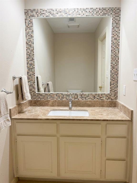 Bathroom vanity featuring white cabinetry, a rectangular undermount sink, stone-finish countertop with matching backsplash, and a large mirror framed by decorative mosaic tile