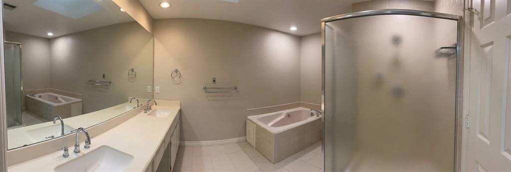 Bathroom featuring a dual-sink vanity with a full-width mirror, a tiled soaking tub, and a separate glass-enclosed shower