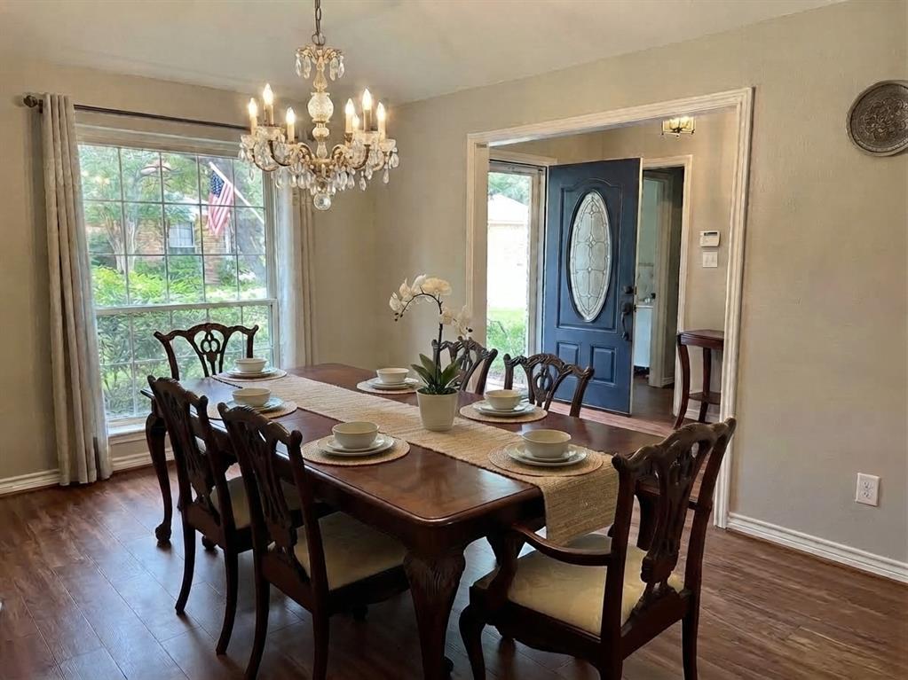 Dining area featuring wood-finish flooring, a multi-light crystal chandelier, a large multi-pane window, and an entry door with an oval glass insert